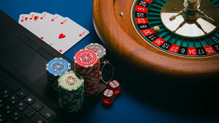 A roulette wheel, poker chips, playing cards, and dice on a laptop keyboard