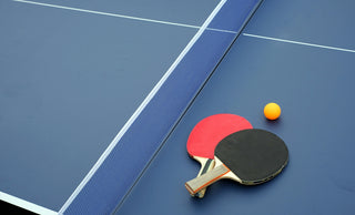 two ping pong paddles and a ping pong ball on a blue table